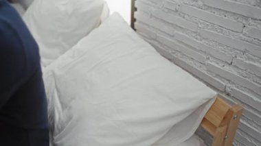 Evdeki yatak odasındaki yatakta dinlenen genç adam gözleri kapalı ve elleri kafasının arkasında tuğla duvar arkasındaydı.