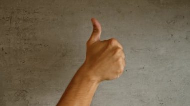 Kaba beton duvarlara karşı baş parmak gösteren adam pozitiflik ve onayı basit ve net bir hareketle veriyor.