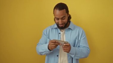 Akıllı telefondaki video oyununu kazanan adam mavi gömlekli parlak sarı arkaplan üzerinden kutluyor..