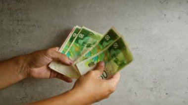 İsrail şekel banknotlarını somut bir zemine karşı sayan eller, tarafsız bir ortamda renkli para birimlerine yakından bakan parmaklar.