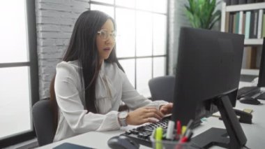 Ofiste çalışan, düşünceli görünen ve akıllı telefon kullanan, modern ofis ekipmanları ve kapalı alan bitkileriyle çevrili bir kadın profesyonel ve sakin bir iş ortamı öneriyor..