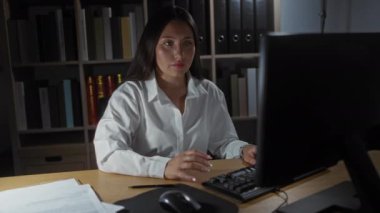 Ofisteki bilgisayarda çalışan genç bir kadın, ev ortamındaki görevlerine odaklanırken notlar alıyor.