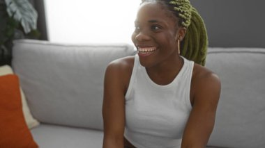 Örgülü bir kadın modern bir apartman dairesinde oturmuş neşeli ve rahat bir atmosfer sergiliyor.