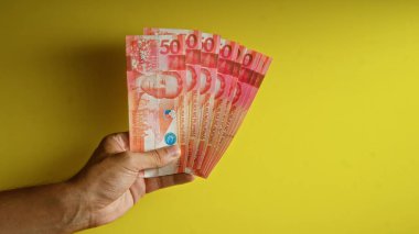 Hand holding multiple philippine peso banknotes against a vibrant yellow background demonstrating wealth and financial concept clipart