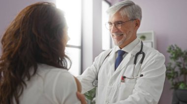 Klinikte kadınlara gülümseyen bir doktor, sağlık hizmetlerini tartışırken, kapalı bir tıbbi ortamda samimiyet ve profesyonellik gösteriyor..