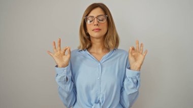Genç bir kadın, sakin bir pozda, gözleri kapalı, mavi gömlekli, izole beyaz bir arka planda meditasyon yapıyor.