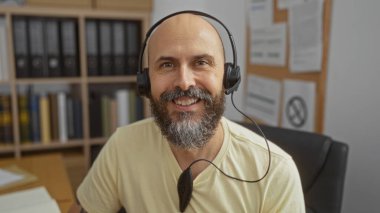 Kapalı ofis ortamında gülümseyen, kulaklık takan yakışıklı İspanyol.