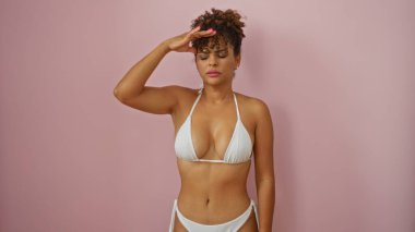 Beyaz bikinili, pembe arka planda poz veren kadın kıvırcık saçlı, kadınlığı, zarafeti ve yaz havasını ön plana çıkaran..