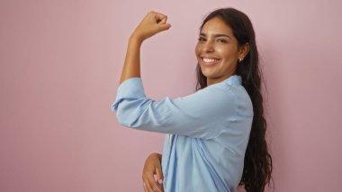 Pembe duvarın önünde gülümseyen ve esneyen bir kadın mavi gömlek giyiyor, güç, güven ve güzellik gösteriyor.