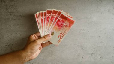 Beton bir zemine karşı sayısız İsrail şekeli banknotlar tutarak renkli para birimini resmediyor.