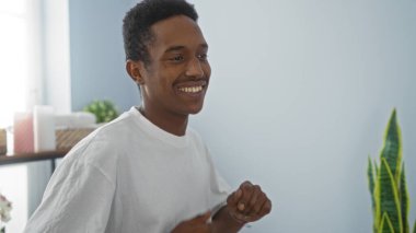 Güzel bir salonun içinde gülümseyen yakışıklı genç adam, sağIıklı dekor ve doğal ışıkla çevrili, rahatlama ve pozitif enerji anı yakalıyor..