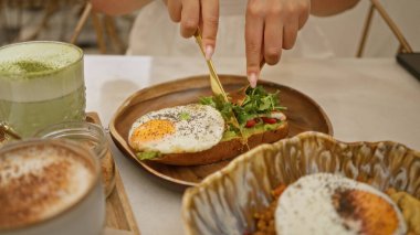 Avokado tostu, kızarmış yumurta ve sıcak bir lokanta masasında matcha latte yiyen bir kadın.