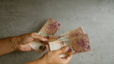 Somut bir zeminde Arjantin pezosu sayan eller.