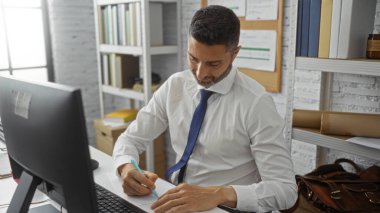 Ofiste çalışan, etrafı kitap ve belgelerle çevrili, beyaz gömlek ve mavi kravat takan İspanyol bir adam, profesyonellik ve çalışkanlığı vurguluyor.