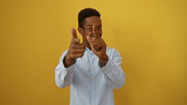 İzole edilmiş sarı arka planda genç ve yakışıklı bir adam güvenle gülümsüyor ve parmaklarıyla işaret ediyor..