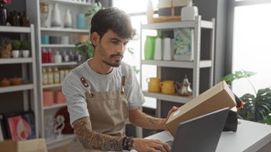 Ev dekorasyonu mağazasında dizüstü bilgisayar ve paket ile çalışan adamın arka planında renkli eşyalar rafları var