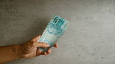Elle tutulur Brezilya 100 reais banknotları somut bir arka plan, sergilenen para, para, finans ve ekonomi kavramları.