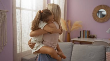 Anne ve kızı sıcak bir kucaklaşmayı paylaşıyor, sıcak, aydınlık bir oturma odasında, kapalı alanda sevgi dolu bir aile anını sergiliyor..
