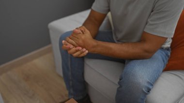 Genç adam bir oturma odasında elleri bağlı, modern bir apartman dairesinde rahat bir şekilde oturuyor ve evinde bir anlık iç gözlem sergiliyor..