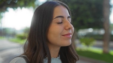 Şehir parkında huzurlu bir anın tadını çıkaran kadın. Kapalı gözleri ve güneş ışığı altındaki sakin ifadesiyle.