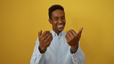 Genç adam bir gülümseme ile davetkar hareketler, canlı sarı bir arka plan üzerinde duran, ışık saçan cazibe ve yakınlık, kendinden emin ve çekici tavrını sergiliyor.