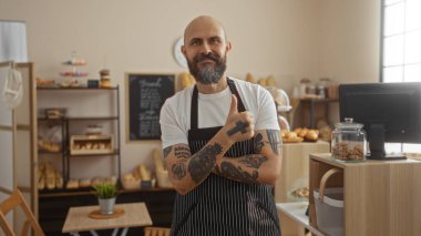 Sakallı yakışıklı İspanyol bir adam arka planda ekmek ve hamur işleri rafları olan samimi bir pastanede güzel bir jest yapıyor.