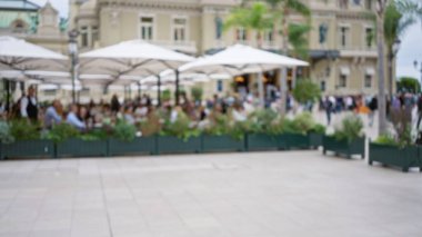Monako 'nun lüks bir caddesinde açık hava şemsiyeleri altında yemek yiyen insanların bulanık görüntüsü, çözünmüş arka planlar ve canlı bir atmosferle bokeh etkisi yaratıyor..
