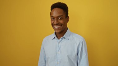 Genç adam rahat ve dostane bir ortamda canlı sarı bir arka plana karşı güvenle gülümsüyor çekicilik ve sıcaklık gösteriyor..