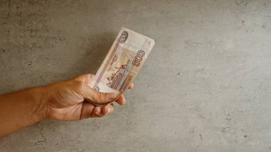 Erkek el, Rusya 'daki mali işlemleri vurgulayan 500 banknot üzerinde yoğunlaşan beton bir zemine karşı Rus rublesi tutuyor.