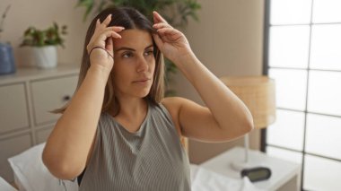 Çekici genç bir kadın sıcak bir yatak odasında, yatağın üzerinde oturuyor.