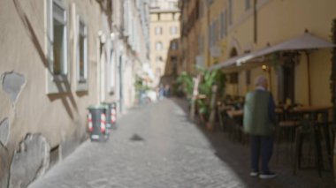 Roma 'da sakin bir kaldırım taşı caddesinde yürüyen bir adamın bulanık binaları ve sakin bir kasaba atmosferini yakalayan açık bir kafe manzarası..