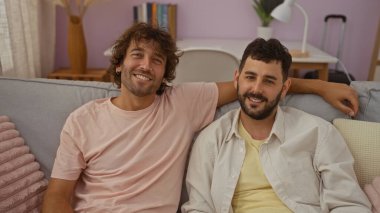 Sıcak bir oturma odasındaki kanepede birlikte oturan erkekler yakın bir bağ gösteriyorlar, arkadaş ya da aile olarak, sıcak ve rahat bir ev ortamında yakalanmışlar..