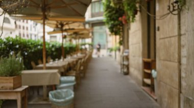 Roma, İtalya 'da güzel bir caddedeki rahat bir açık hava kafenin bulanık manzarası. Parlak bir gökyüzünün altında çözülmüş masalar ve şemsiyeler sergileniyor..