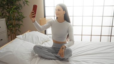 Yatak odasında, camdan süzülen doğal ışıkla selfie çeken bir kadın.