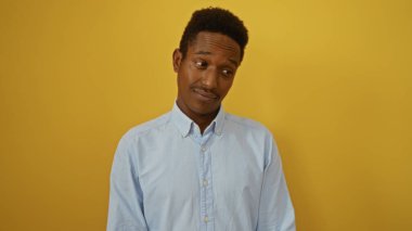 İzole edilmiş sarı bir arka plana poz veren Afro-Amerikalı genç bir adam kendinden emin ve çekici bir varlık sergiliyor..