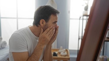 Adamın biri kaplıcada sakin bir şekilde yüzünü inceliyor. Sağlık merkezindeki rutin cilt bakımını, dingin bir ortam ve olgun özbakım ortamını gösteriyor..