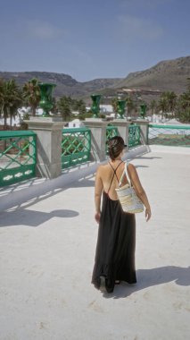 Lanzarote kanarya adalarında açık havada siyah elbiseler giyen genç bir kadın. Etrafı palmiye ağaçları ve güneşli gökyüzünün altında dağlarla çevrili yürüyor.
