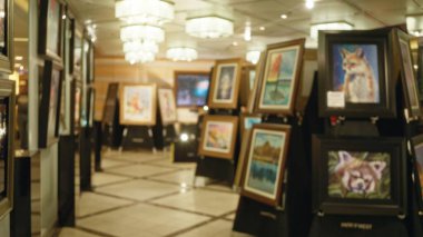 Arka planda bulanık tablolarla dolu sanat galerisi iyi aydınlatılmış modern bir ortamda canlı sanatsal ifadeler sergiliyor..