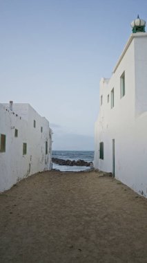 Beyaz binalar arasında uzanan dar kumlu yollar açık gün ışığında Lanzarote 'deki famara plajına, kanarya adalarına çıkar.
