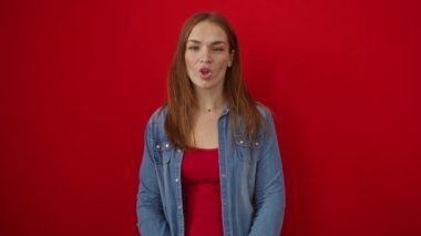 Parlak kırmızı arka planda gülümseyen bir kadın, günlük kot ceketiyle, promosyon malzemesi için izole bir ortamda genç ve neşeli bir hava sergiliyor.