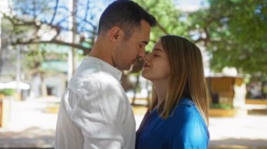 Erkek ve kadın, arka planda ağaçlar ve binalarla dolu güneşli bir şehir parkında, mutluluğu ve birlikteliği resmeden romantik bir anı paylaşıyorlar..