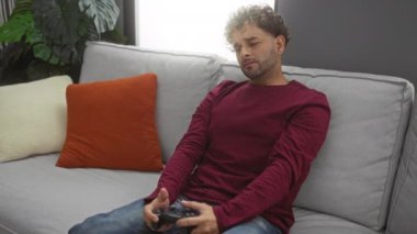 Genç adam rahat bir oturma odasında yastıklarla kapalı bir koltukta oynuyor.
