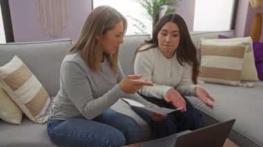 Anne ve kızı evdeki bir kanepede oturmuş, ciddi bir şey tartışıyorlar. Evraklar ve dizüstü bilgisayarla, sıcak bir oturma odasında aile anı sergiliyorlar..