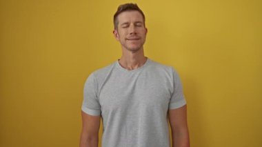 Neşeli sarı arka planda yalnız gülümseyen genç bir adam. Günlük gri gömlek giyiyor. Kendine güveni ve pozitifliği ifade ediyor.