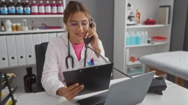 Kadın doktor hastane ofisinde telefonla konuşurken bilgisayarın yanındaki tablet üzerinde tıbbi malzemelerle birlikte evrakları gözden geçiriyordu.