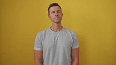 Gri tişörtlü genç adam, parlak sarı bir arka plana karşı duruyor. Kendine güveni tam. Yüzünde güzel bir ifade ve sıradan bir tarz var.