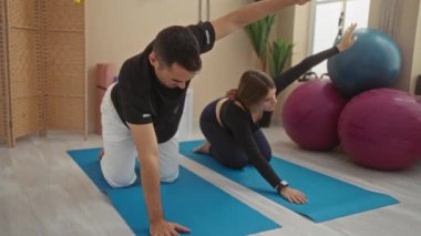 Erkek ve kadın, arka planda yoga topları, spor salonunda paspaslarla yoga yapıyor. Spor salonu zemininde zindelik, esneklik ve sağlıklı bir yaşam tarzı var..