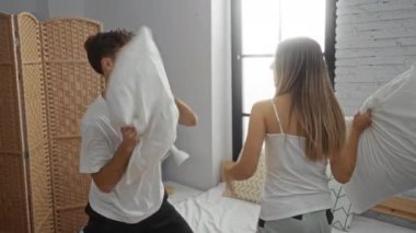 Bir çift, rahat, modern bir yatak odasında bir yastık savaşında, bir erkekle bir kadın arasında eğlenceli ve samimi bir anı yakalıyor..