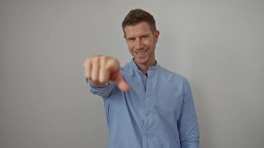 Genç adam kameraya özgüvenle bakıyor, beyaz arka planda gülümsüyor, tercihi ve müdahaleyi öneriyor, günlük mavi gömlek giyiyor, izole edilmiş ve çekici.