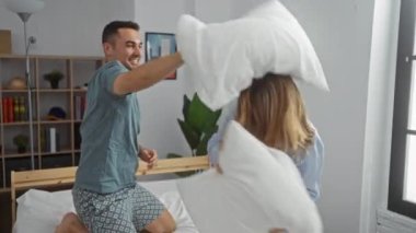 Yatak odasındaki rahat yatakta şakacı bir yastık kavgası. Modern bir ev ortamında ilişki dinamikleri, kahkahalar ve samimiyet sergiliyor..
